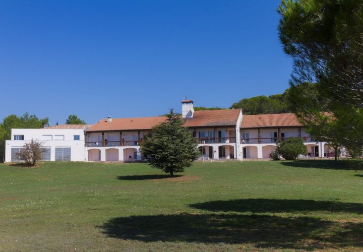 Une grande maison blanche au milieu d’un champ herbeux.