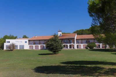 Une grande maison blanche au milieu d’un champ herbeux.