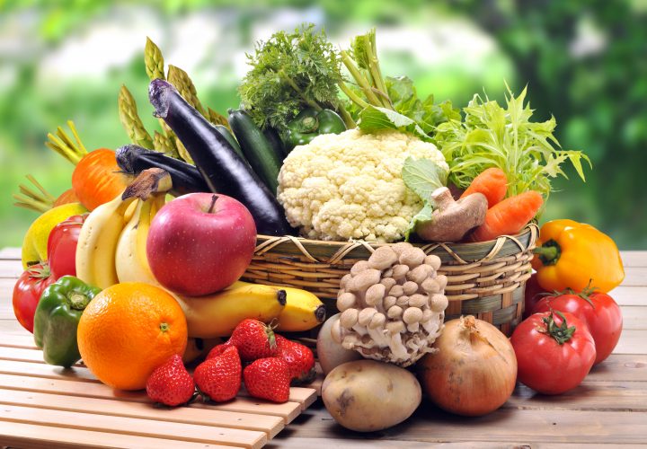 Un panier plein de fruits et légumes sur une table en bois.