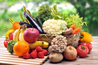 Un panier plein de fruits et légumes sur une table en bois.