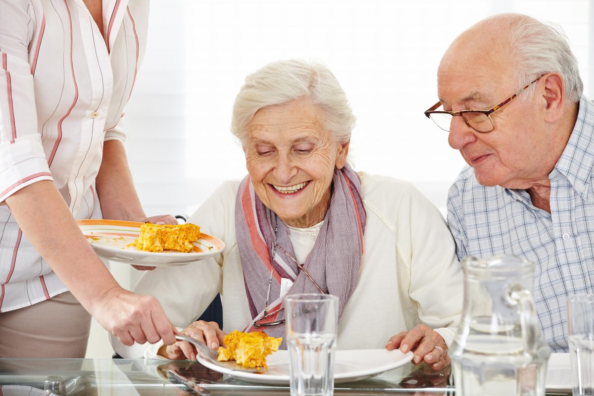 Une femme sert une assiette de nourriture à un couple de personnes âgées.