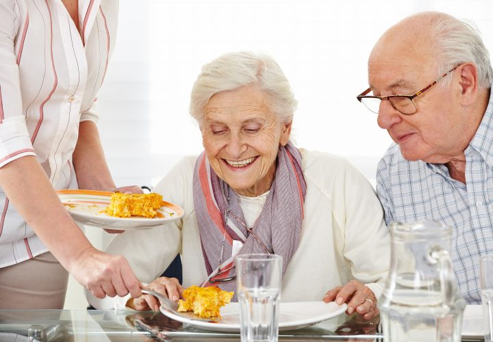 Une femme sert une assiette de nourriture à un couple de personnes âgées.