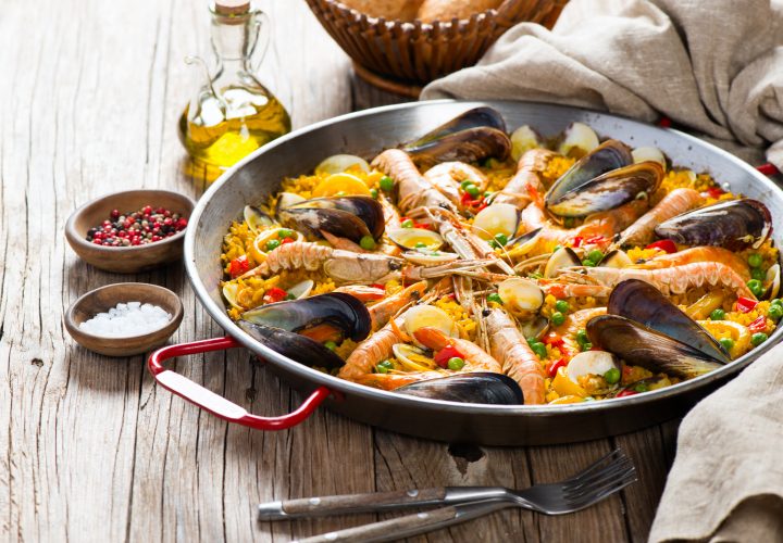 Paella aux fruits de mer et légumes dans une poêle sur une table en bois.