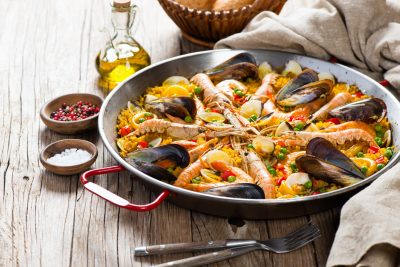 Paella aux fruits de mer et légumes dans une poêle sur une table en bois.