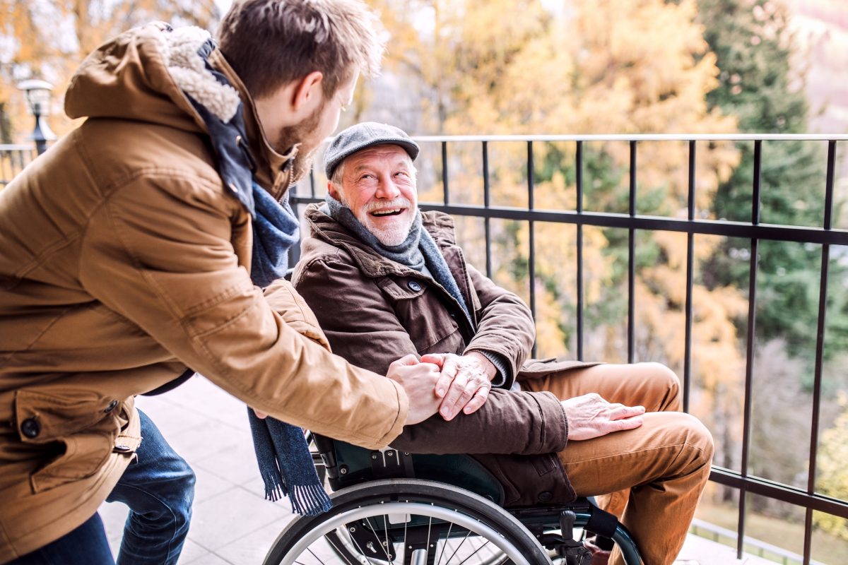 Un homme âgé en fauteuil roulant est aidé par un jeune homme.
