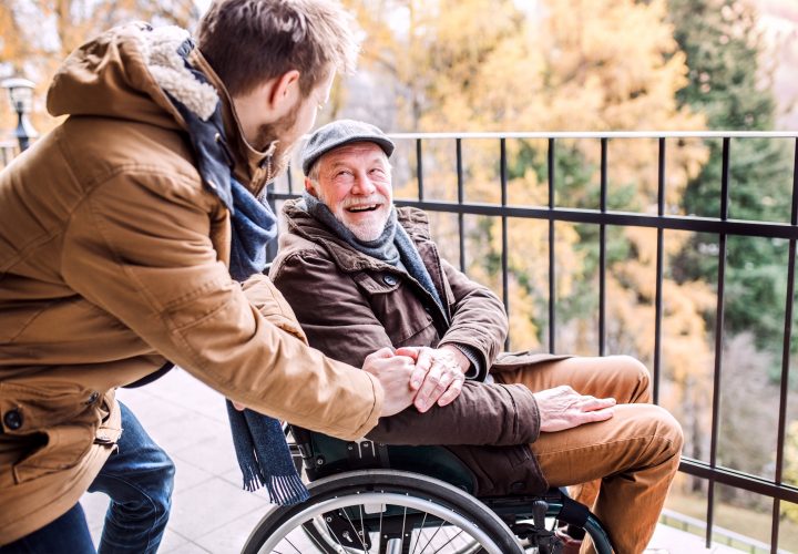 Un homme âgé en fauteuil roulant est aidé par un jeune homme.