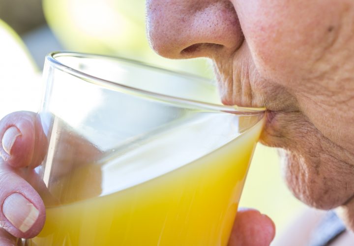 Une femme boit du jus d’orange dans un verre.