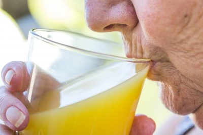 Une femme boit du jus d’orange dans un verre.