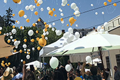 Des ballons blancs et jaunes flottent au-dessus d’une foule de personnes.