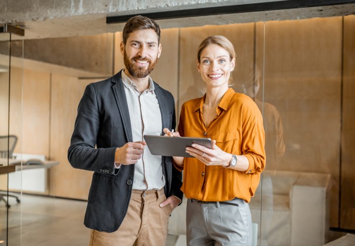 Un homme d'affaires et une femme debout dans un bureau tenant une tablette.