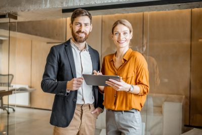Un homme d'affaires et une femme debout dans un bureau tenant une tablette.