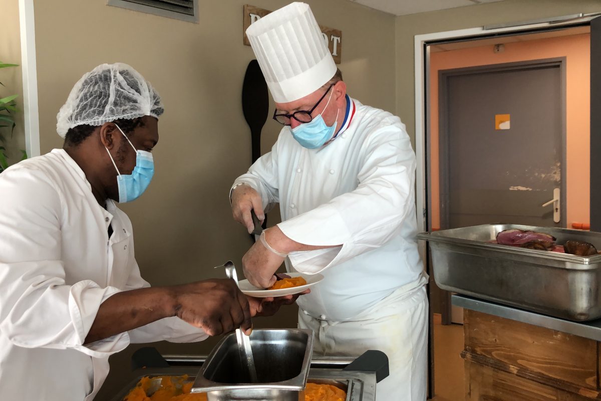 Deux hommes masqués préparant de la nourriture dans une cuisine.