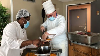 Deux hommes masqués préparant de la nourriture dans une cuisine.