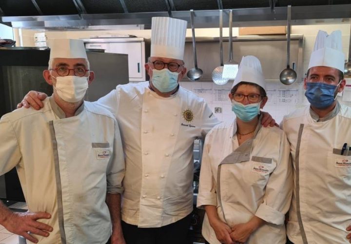 Quatre chefs portant des masques dans une cuisine.