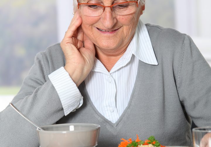 Une femme âgée mange une assiette de nourriture.