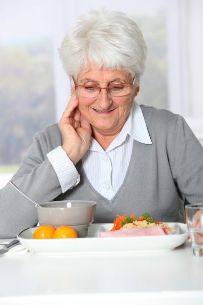 Une femme âgée mange une assiette de nourriture.