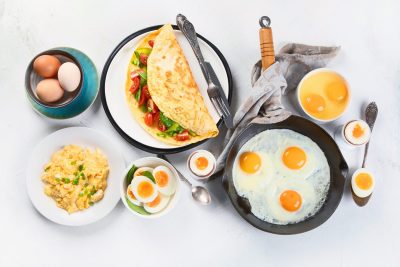 Omelette, œufs, crêpes et autres aliments pour le petit-déjeuner sur fond blanc.