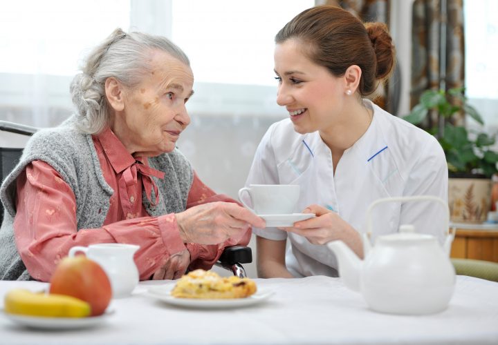 Une infirmière discute avec une femme âgée assise à une table.