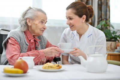 Une infirmière discute avec une femme âgée assise à une table.