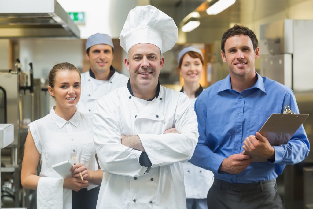 Un groupe de chefs réunis dans une cuisine, formulant des offres de restauration pour maisons de retraite.