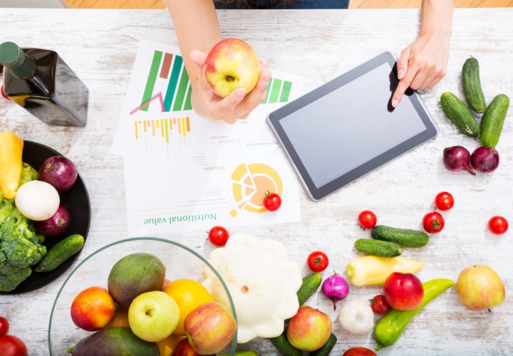 Une femme utilise une tablette entourée de fruits et de légumes.