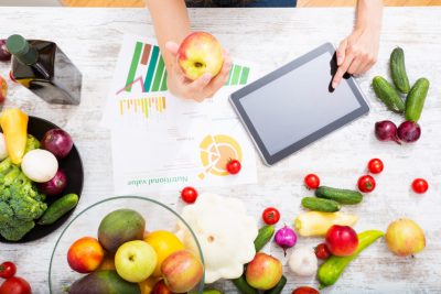 Une femme utilise une tablette entourée de fruits et de légumes.