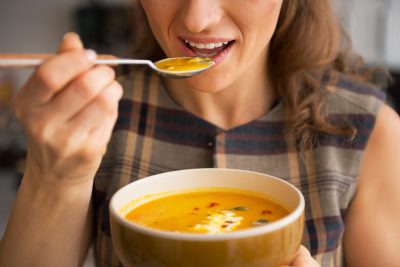 Une femme mange un bol de soupe avec une cuillère.