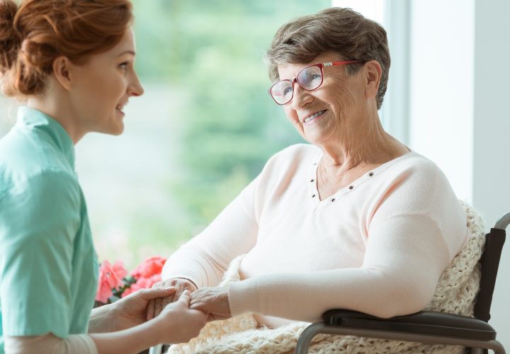 Une infirmière parle à une femme âgée en fauteuil roulant.