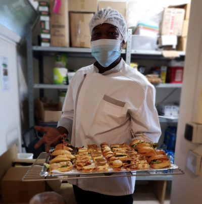 Un homme masqué tenant un plateau de sandwichs.