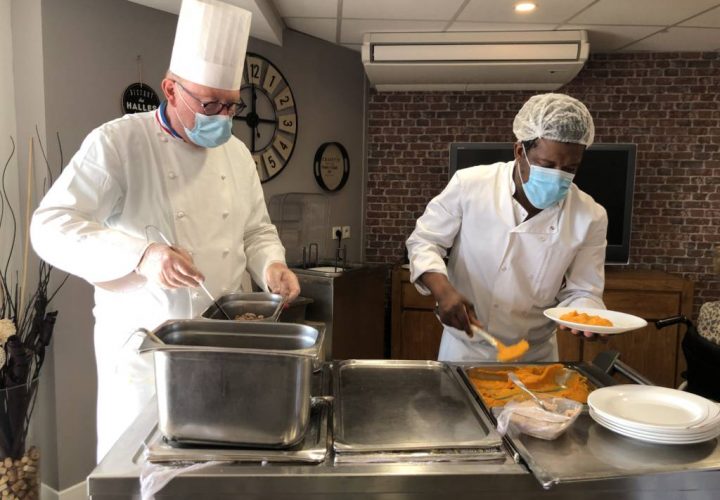 Deux hommes masqués préparant de la nourriture dans une cuisine.