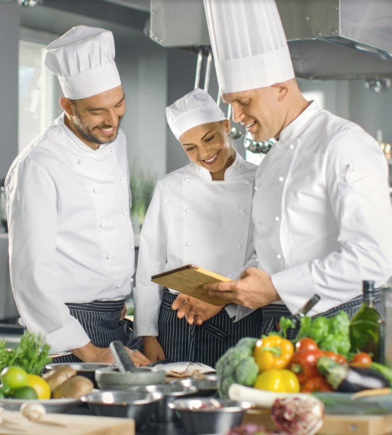 Trois chefs experts de la restauration collective pour les maisons de retraite et EHPAD regardent une tablette dans une cuisine.