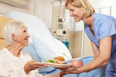 Une infirmière sert de la nourriture à une femme âgée dans un lit d'hôpital.