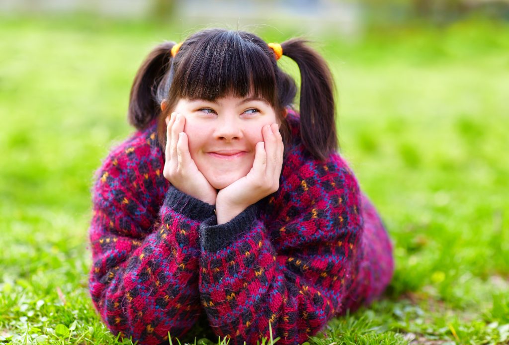 Une fille étendue sur l'herbe avec ses mains sur son visage, rêvant de restauration pour établissements accueillant des personnes en situation de handicap.