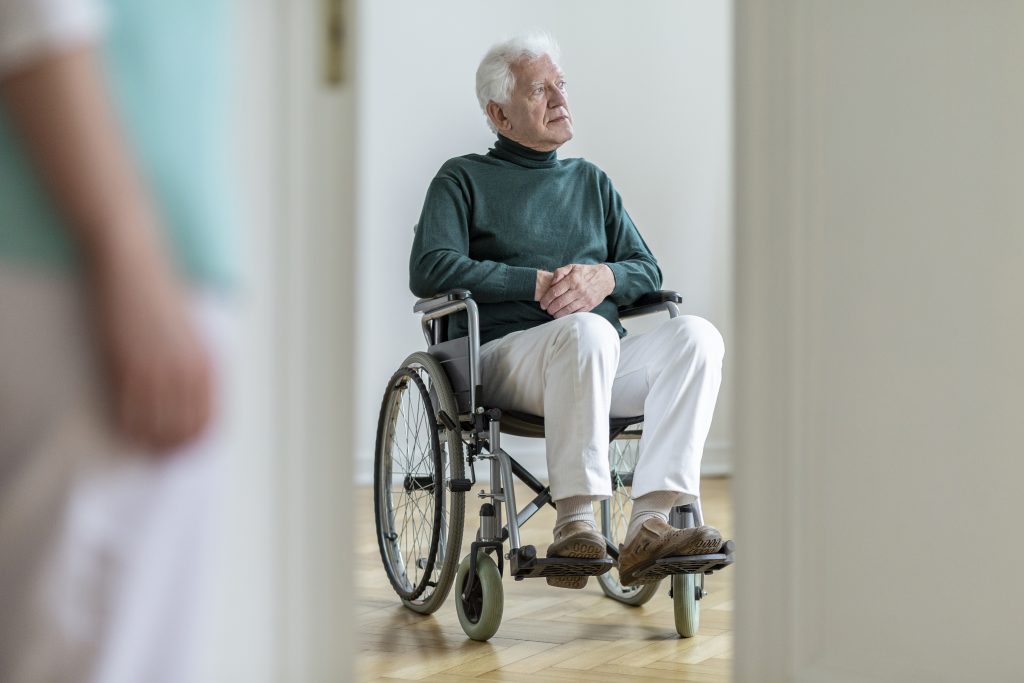 Un homme âgé en fauteuil roulant regardant par la porte d'un restaurant pour établissements accueillant des personnes en situation de handicap.