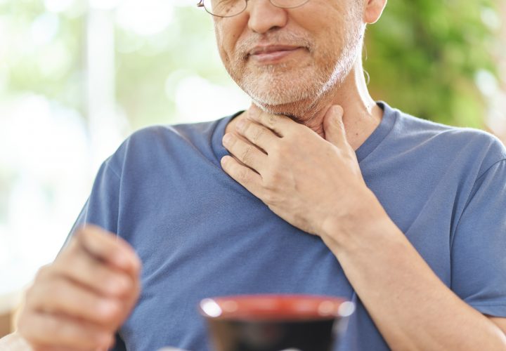 Un homme se tient le cou en mangeant une tasse de café.