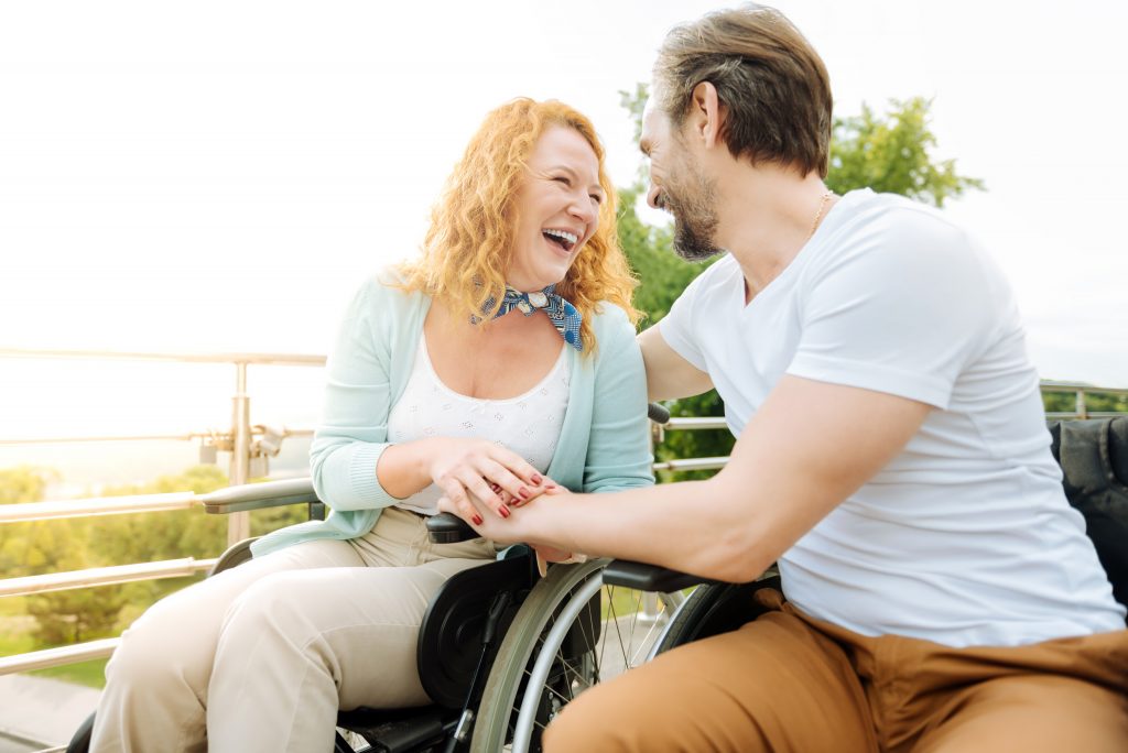 Un homme et une femme en fauteuil roulant rient dans l'espace de restauration d'un établissement pour personnes handicapées.