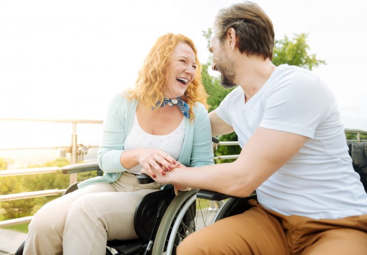 Un homme et une femme en fauteuil roulant rient dans l'espace de restauration d'un établissement pour personnes handicapées.