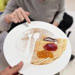 Une femme tient une assiette de crêpes avec de la confiture dessus.