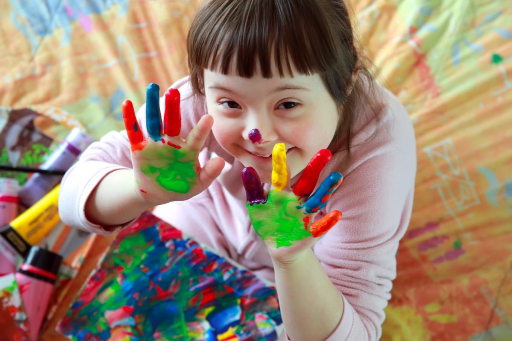 Une jeune fille avec de la peinture colorée sur les mains participe à un atelier de restauration d'établissements accueillant des personnes handicapées.