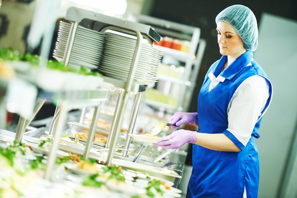 Une femme en uniforme bleu prépare de la nourriture sous forme de buffet.