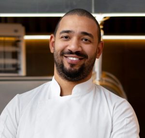 Un homme en uniforme de chef blanc souriant.