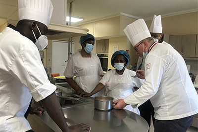 Un groupe de chefs préparant des plats dans une cuisine pour une prestation restauration VITALREST qui s’adapte aux besoins de l’EHPAD.