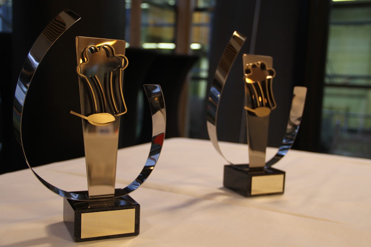 Deux trophées sur une table devant une fenêtre.