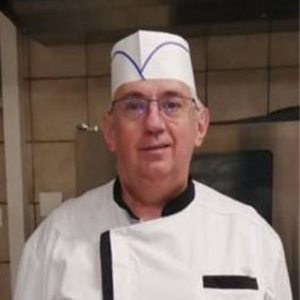 Un homme en uniforme de chef debout dans une cuisine.