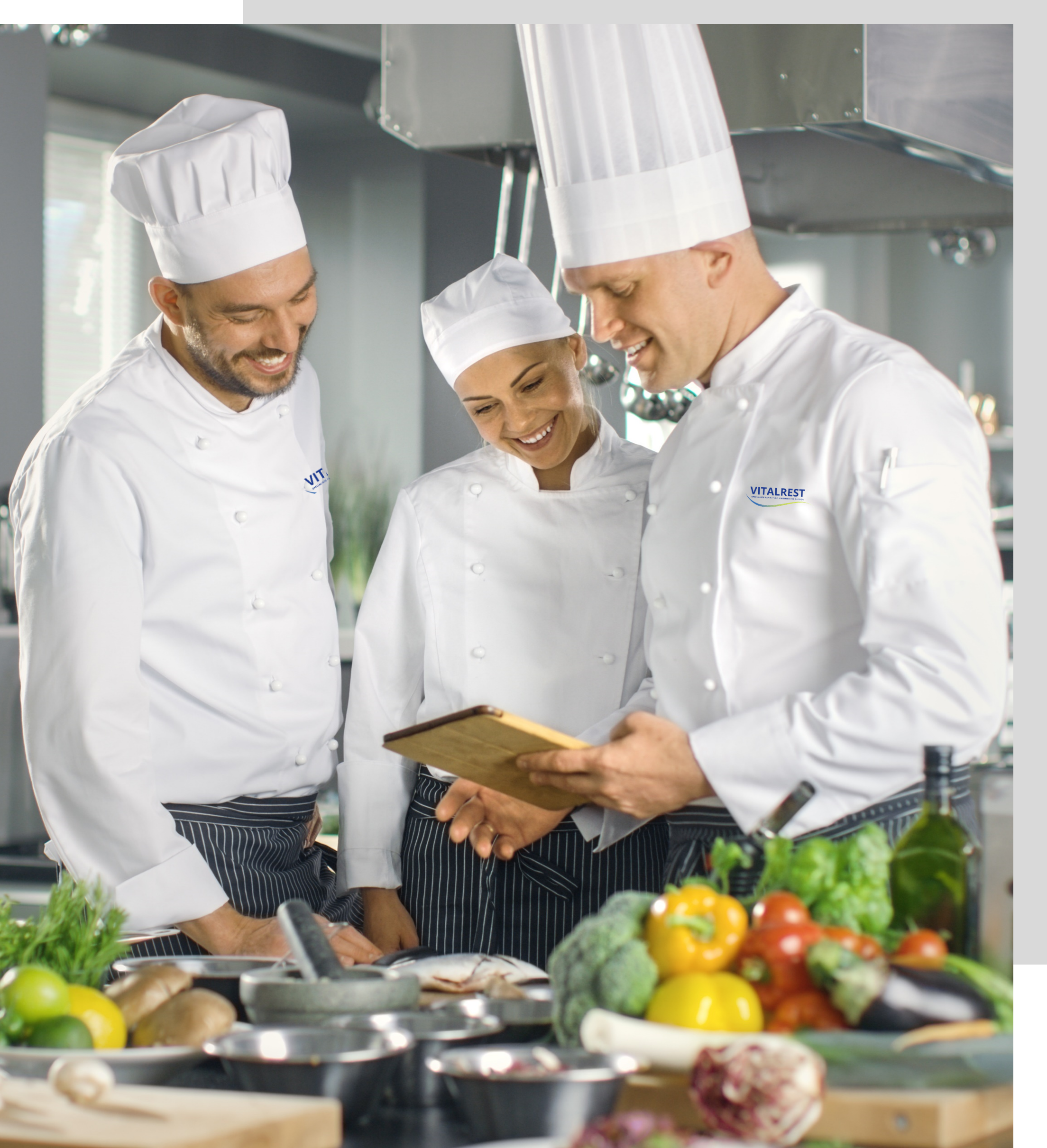 Trois chefs regardant une tablette dans une cuisine.