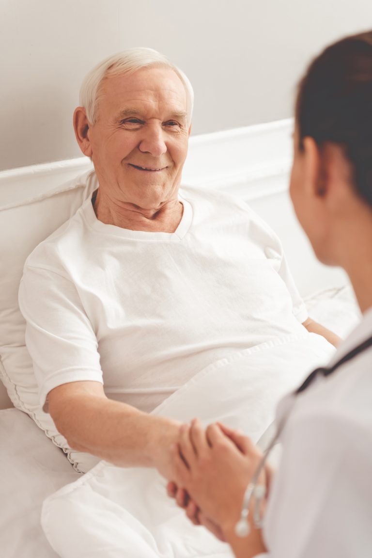 Une infirmière serre la main d’un homme âgé dans un lit d’hôpital.