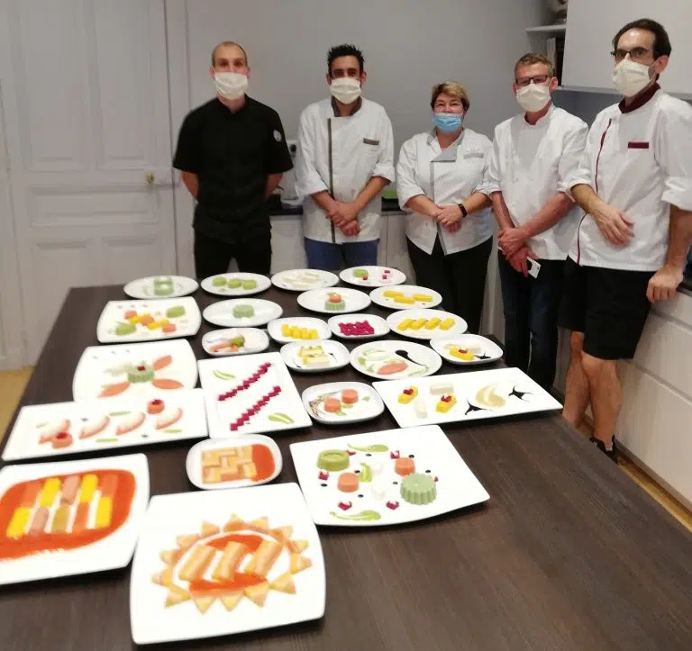 Un groupe de chefs posant devant des assiettes de nourriture.