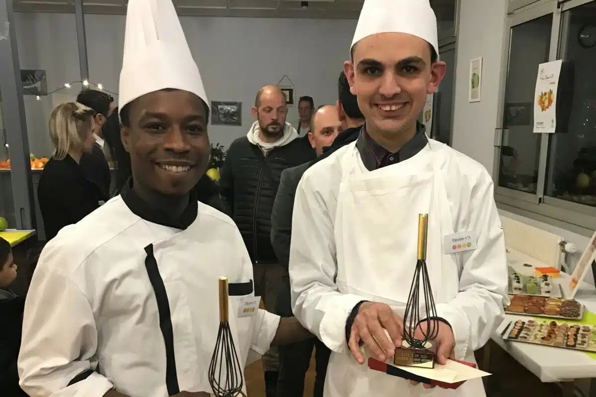 Deux chefs participants à un concours culinaire pour les personnes en situation de handicap, posant pour une photo dans une cuisine.