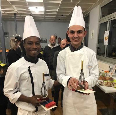 Deux chefs participants à un concours culinaire pour les personnes en situation de handicap, posant pour une photo dans une cuisine.