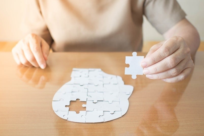 Une femme tient sur une table une pièce de puzzle, symbolisant l'adaptation quotidienne de l'alimentation des patients atteints de la maladie d'Alzheimer.